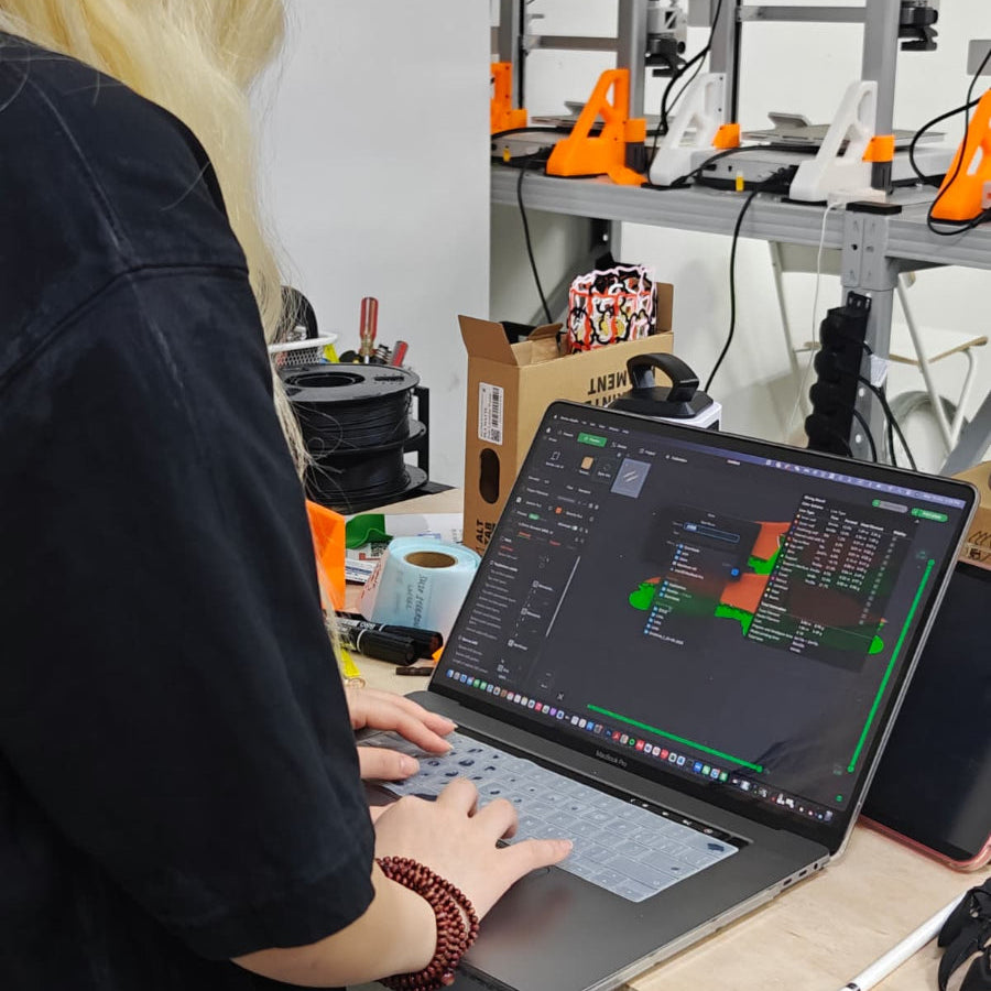Person using a laptop in a workshop with 3D printers in the background