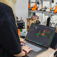 Person using a laptop in a workshop with 3D printers in the background